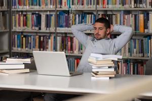 A male college student in a library looking at his laptop 