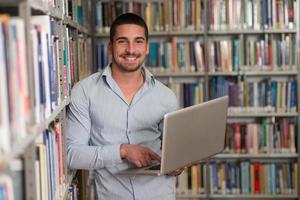 feliz estudiante masculino con laptop en biblioteca foto