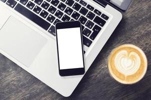 Blank smartphone on laptop with cup of coffee photo