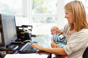 A mother holding her baby and working from home photo