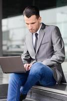 Young businessman typing in a laptop computer in urban backgroun photo
