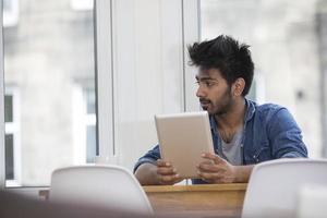 Hombre asiático sentado en una mesa leyendo un tablet pc.