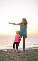 Fit young mother pointing into distance for daughter on beach