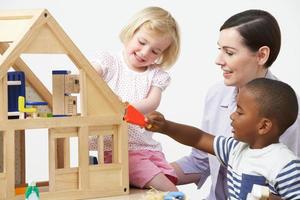 Pre-School Teacher And Pupils Playing With Wooden House photo