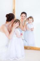 hermosa madre e hija adorable niño probándose vestidos blancos