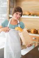 Pretty waitress putting croissant in paper bag