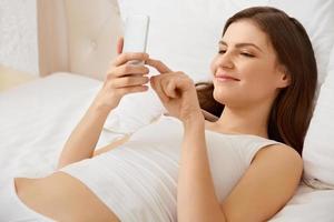 Retrato de mujer feliz acostada en la cama con teléfono inteligente foto
