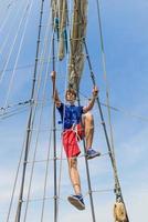 Young sailor climbing on mast of tall ship.