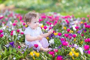lindo y pequeño bebé rizado sentado entre hermosas flores de primavera foto