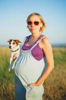 Happy pregnant woman with a dog at sunset