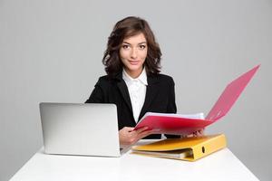secretaria bastante segura trabajando con computadora y carpetas coloridas foto