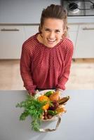 Woman in kitchen looking up holding bag of fall veggies