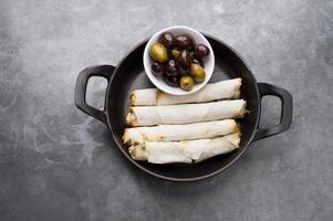 Cheese rolls plate with olives served in a black pan photo