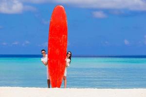 Young couple with red surfboard on white beach photo