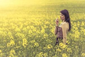 Beautiful woman in meadow of yellow flowers enjoying flower
