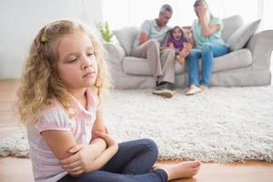 Upset girl sitting on floor while parents enjoying with brother