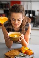 mujer joven disfrutando de sopa de calabaza en la cocina foto