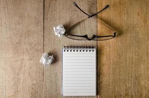 Blank notepad and eye glasses on wooden table photo