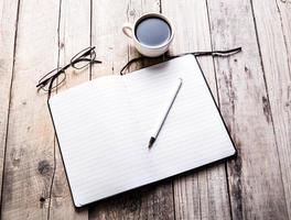 glasses on notebook with pen and cup of coffee