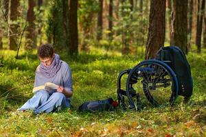 Disabled woman reading a book in the forest, wheelchair