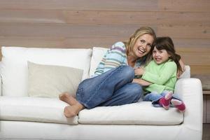 Mother and daughter sitting on sofa embracing smiling