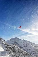 Helicóptero rojo en vuelo en los Alpes de invierno con nieve en polvo foto