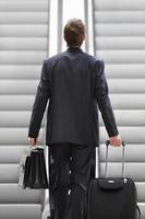 Businessman on escalator with bag and trolley photo