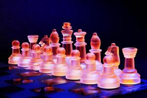 Glass chess on chessboard lit by blue and orange light photo
