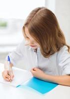 Chica estudiante escribiendo en el cuaderno en la escuela foto