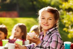Smiling girl holds cupcake with her friends behind photo