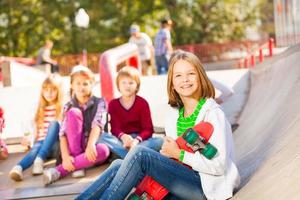 Girl sits in front with skateboard and other kids photo