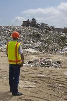 Worker watching digger moving waste at landfill site photo
