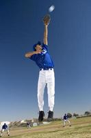 Baseball player, in blue uniform, jumping up to catch ball