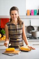 Elegant woman in kitchen smiling while putting butter on corncob photo