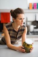 Elegant woman leaning on kitchen counter holding jar of pickles