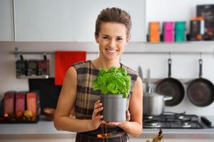 Smiling woman in kitchen holding pot of fresh basil