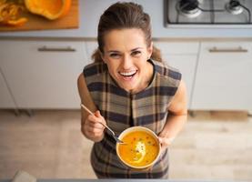 portrait of happy young housewife eating pumpkin soup