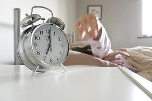 Sleepy woman reaching to turn off alarm clock photo