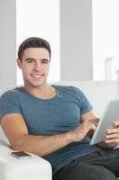 Cheerful handsome man relaxing on couch using tablet photo