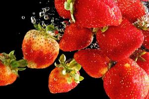 Strawberries falling into water at black background