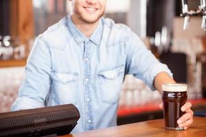 Cheerful young male bartender is serving customer in pub photo