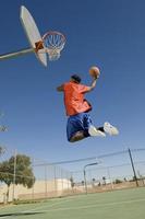 Hombre mojando el baloncesto en el aro contra el cielo azul foto