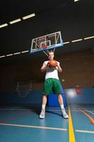Hombre joven sano y duro jugando baloncesto en el gimnasio interior. foto