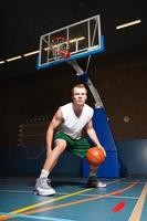 Hombre joven sano y duro jugando baloncesto en el gimnasio interior. foto