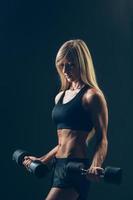 Athletic woman with dumbbells on a dark background