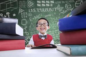 Asian boy laughing in class with stack of books photo