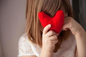 Chica escondida detrás de un corazón rojo de punto, el día de San Valentín, foto