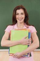 Teacher standing in front of chalkboard holding files smiling photo