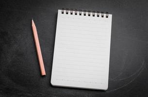 Open Blank notepad on  black chalkboard background with pencil photo
