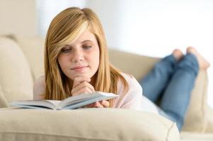 Young student girl reading book on sofa